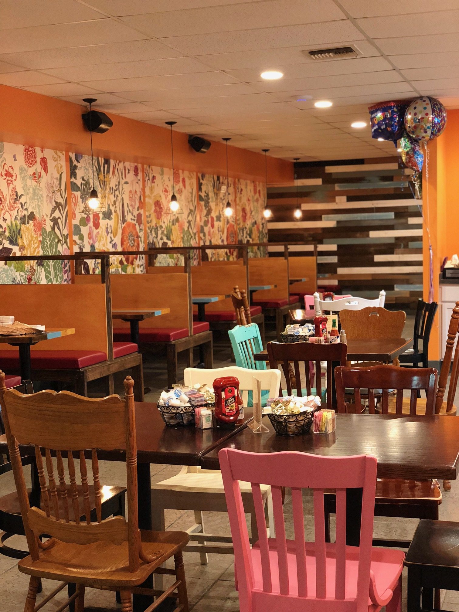 Dining room with floral wallpaper, pendant lights and colorful mismatched chairs